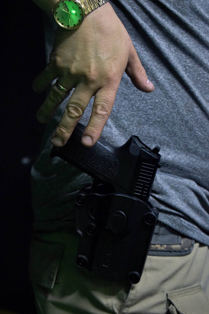 Hand with a watch resting on a holstered gun. Close-up shot emphasizing security and readiness.